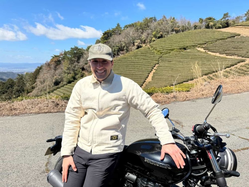 Smiling rider with a Honda motorcycle parked on a mountain road, representing everyday riders and affordable coverage options