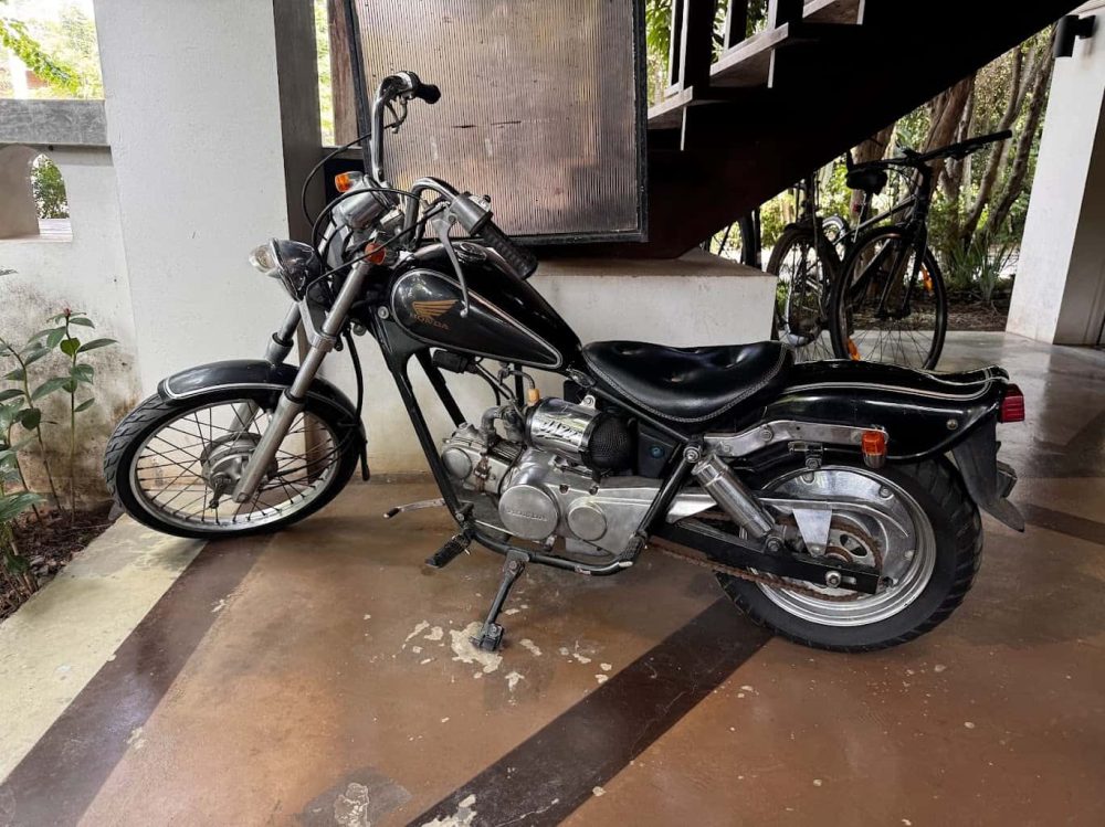 Old black Honda motorcycle parked in storage under a staircase