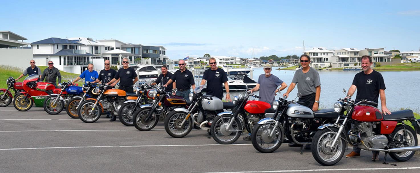Group of classic motorcycle riders posing with vintage bikes near the waterfront