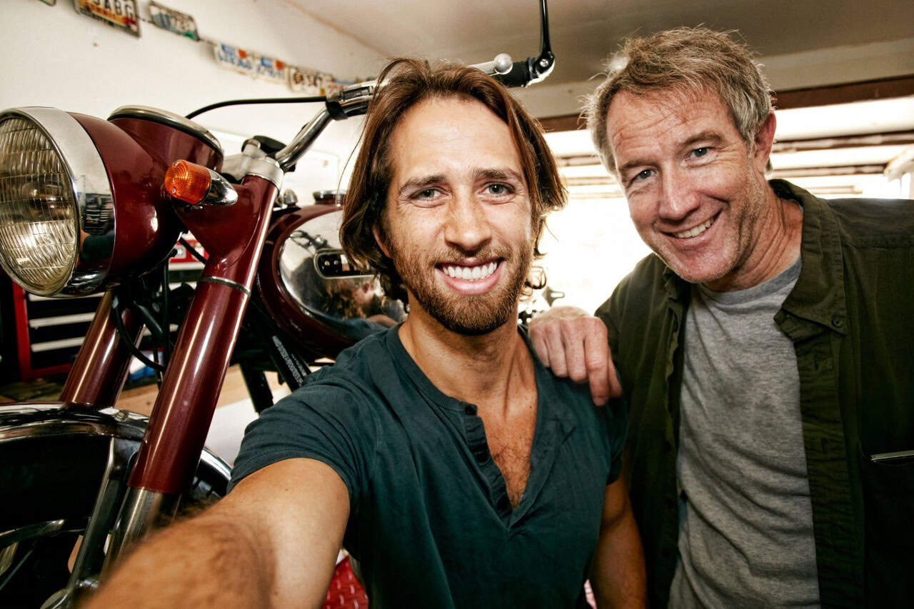 Two smiling motorcyclists in a garage with a vintage bike, representing how experience and training build riding confidence.