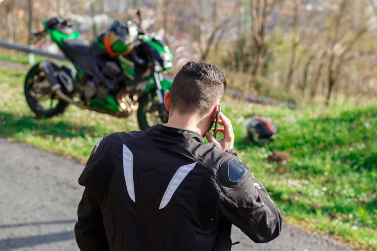 Motorcyclist making a phone call beside a parked bike on a rural roadside