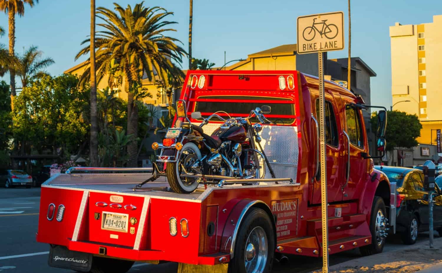 Classic motorcycle loaded on a red tow truck under palm trees at sunset