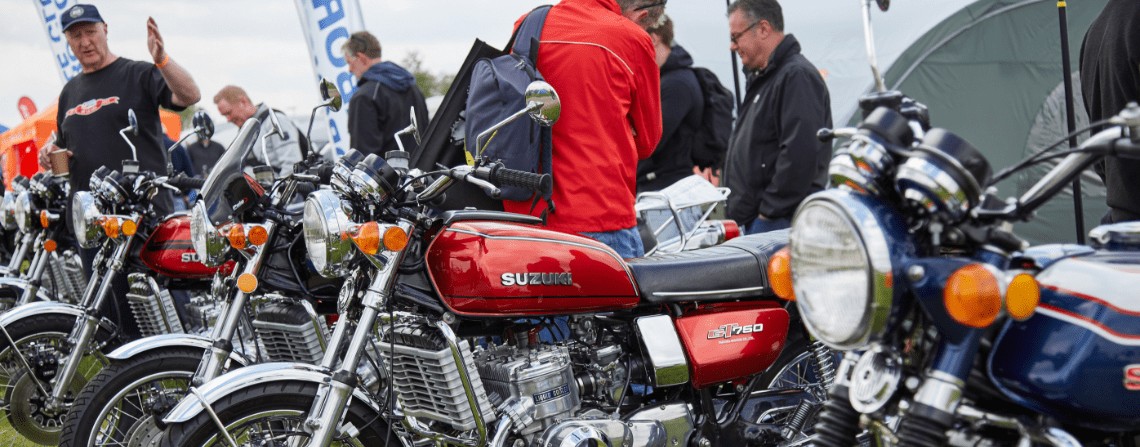 Riders gather at a classic motorcycle show featuring vintage Suzuki GT750s