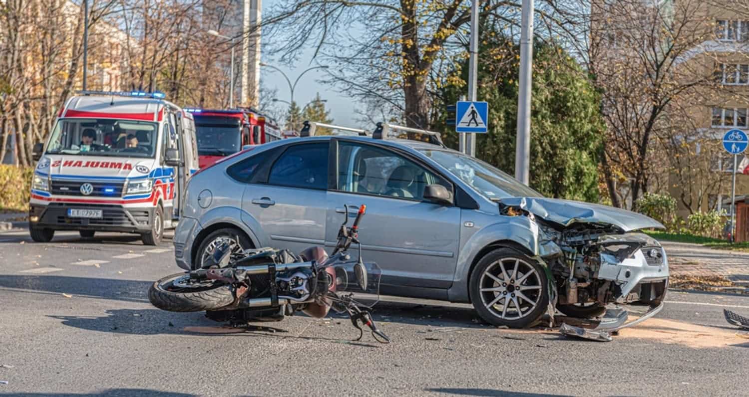 Motorcycle and car collision on a city street with emergency responders arriving at the scene.