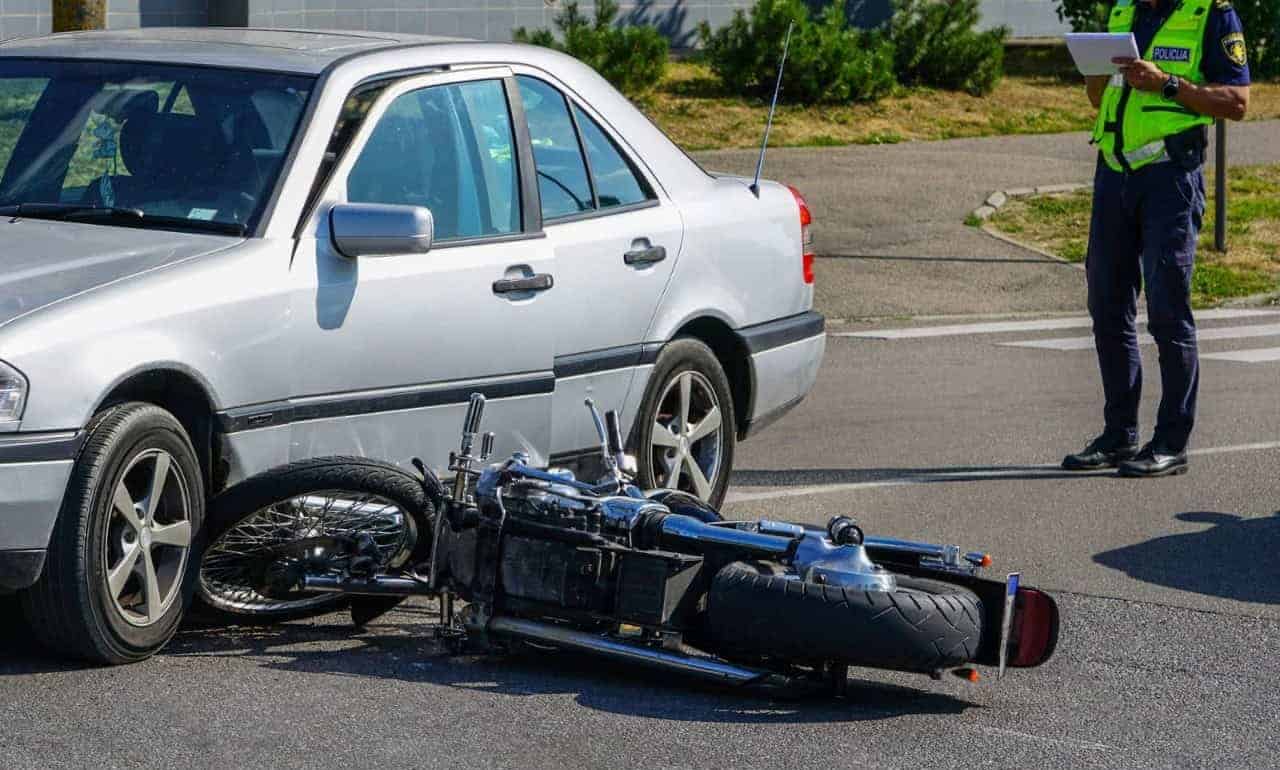 Motorcycle accident involving a car with a police officer taking notes at the scene