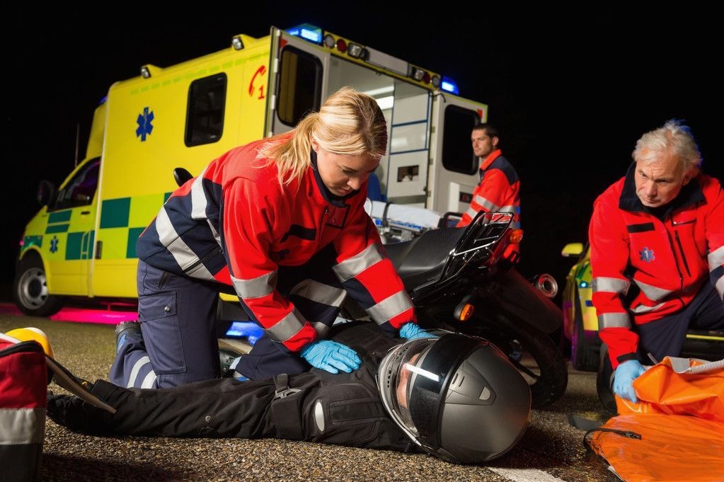 Paramedics assisting an injured motorcyclist after an accident beside an ambulance at night