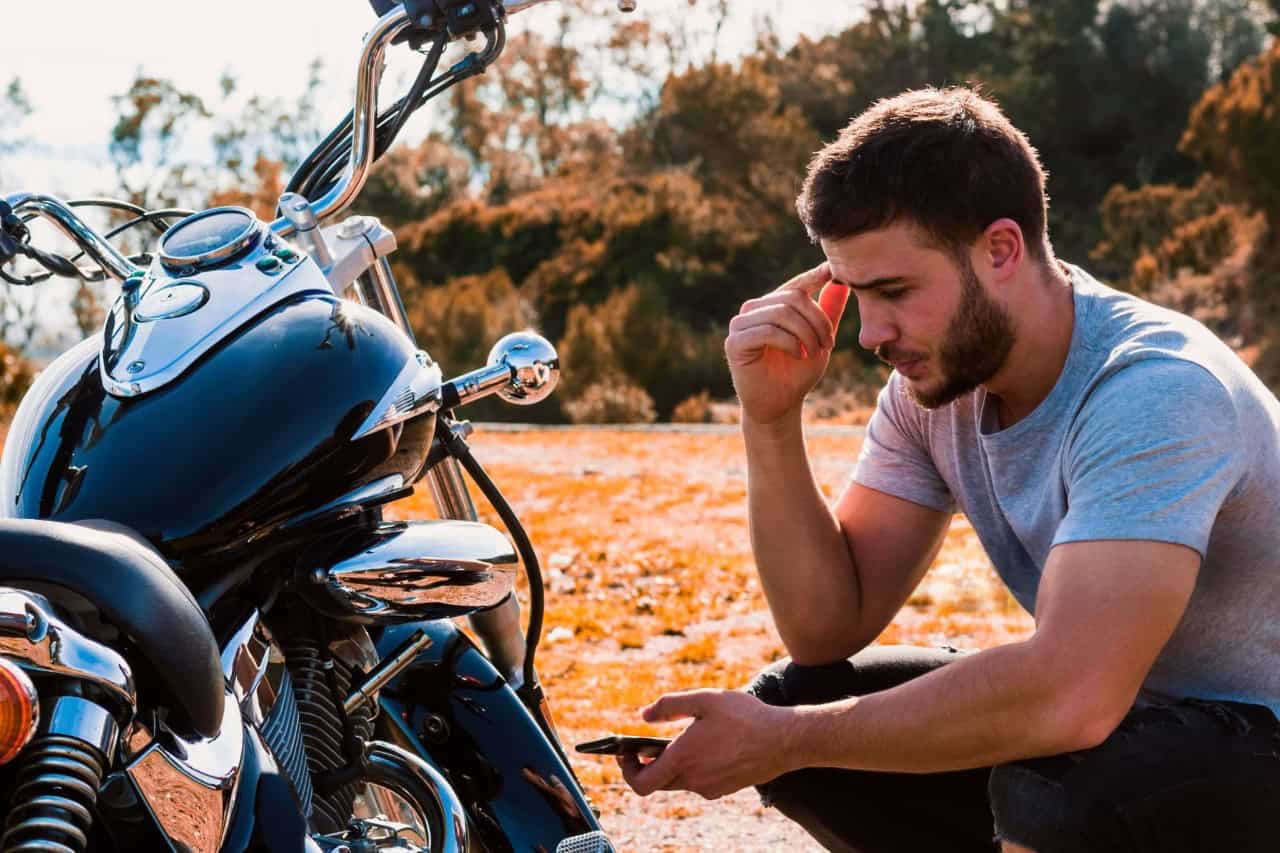 Motorcyclist sitting beside his bike, checking his phone—represents choosing add-ons like roadside assistance or gear coverage.
