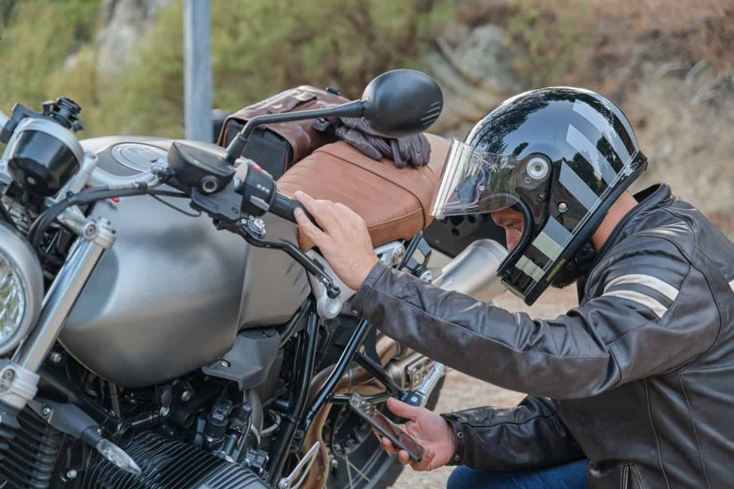 Motorcyclist checking a stalled bike and using a phone to request roadside help