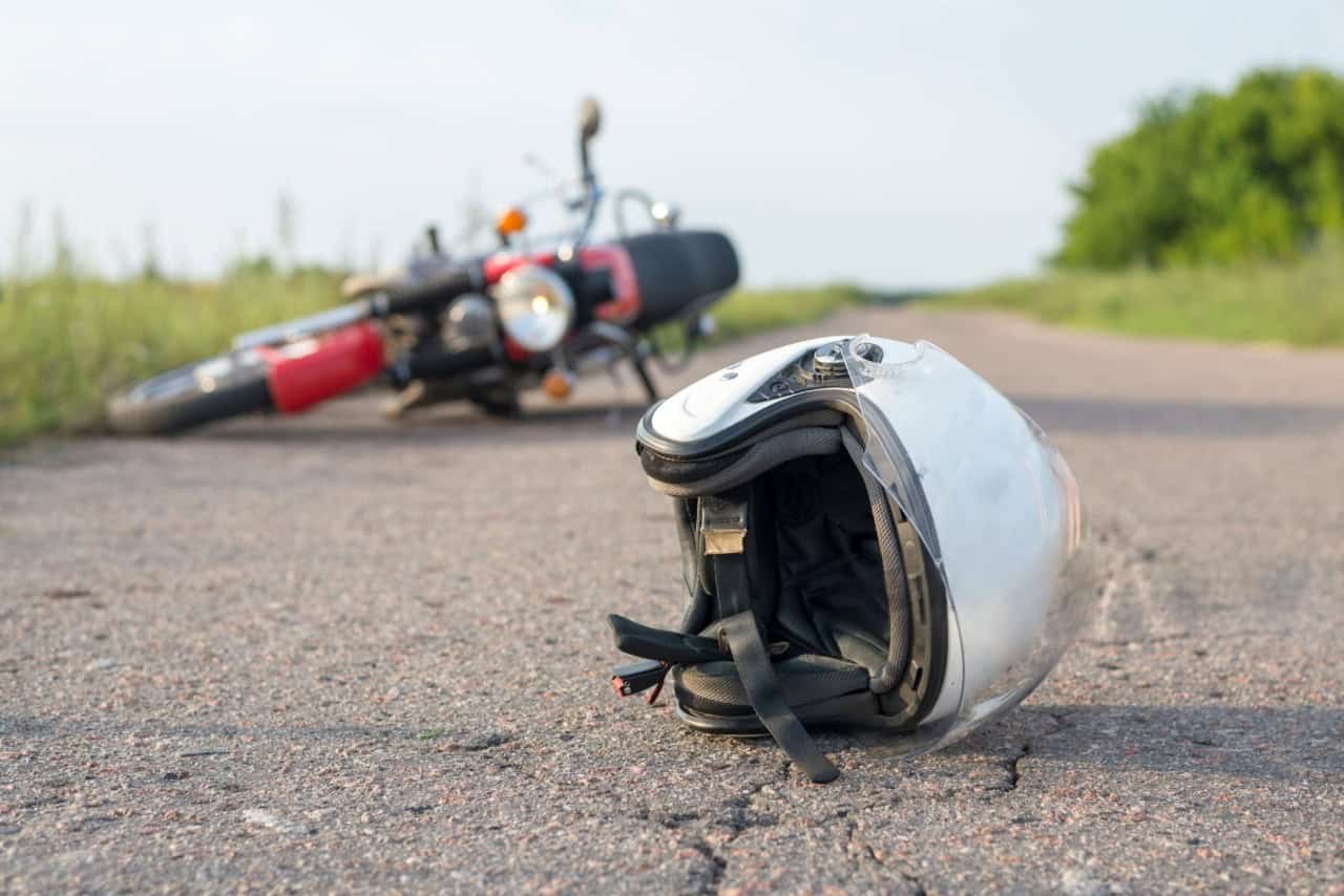 Motorcycle helmet on road after an accident with a crashed bike in the background