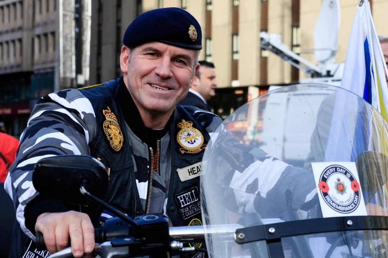 Smiling military veteran on a motorcycle wearing a decorated jacket and beret, symbolizing GEICO’s support for service members.