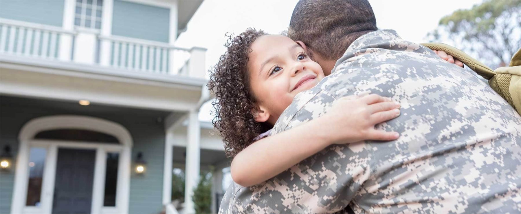 Military parent in uniform hugging a child outside their home, representing family protection with Armed Forces Insurance.