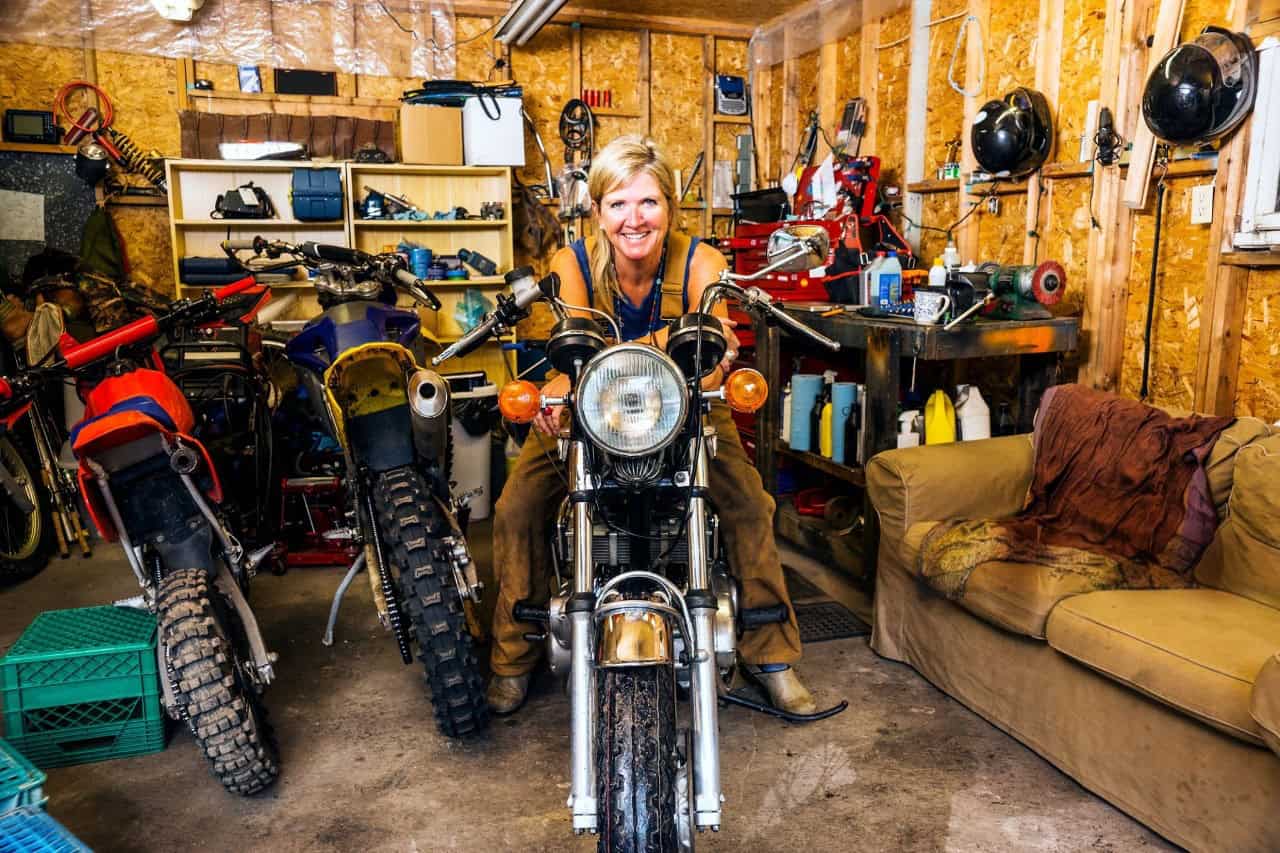 Rider in a garage surrounded by multiple motorcycles and tools