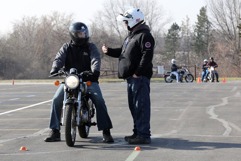 Motorcycle instructor coaching a new rider during a safety course on a training lot, emphasizing rider education and safety