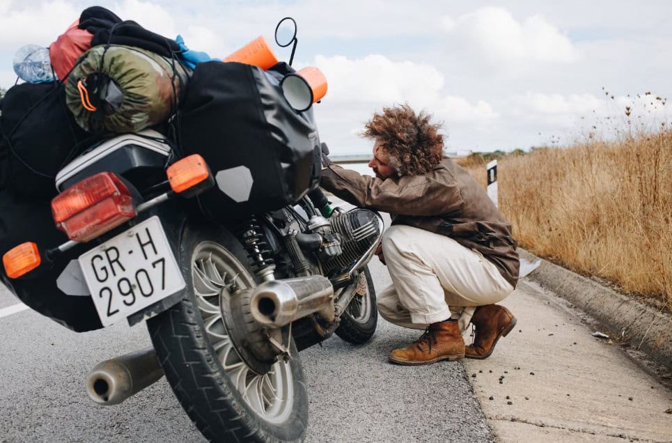 Motorcyclist fixing a breakdown on the roadside beside a fully loaded touring bike