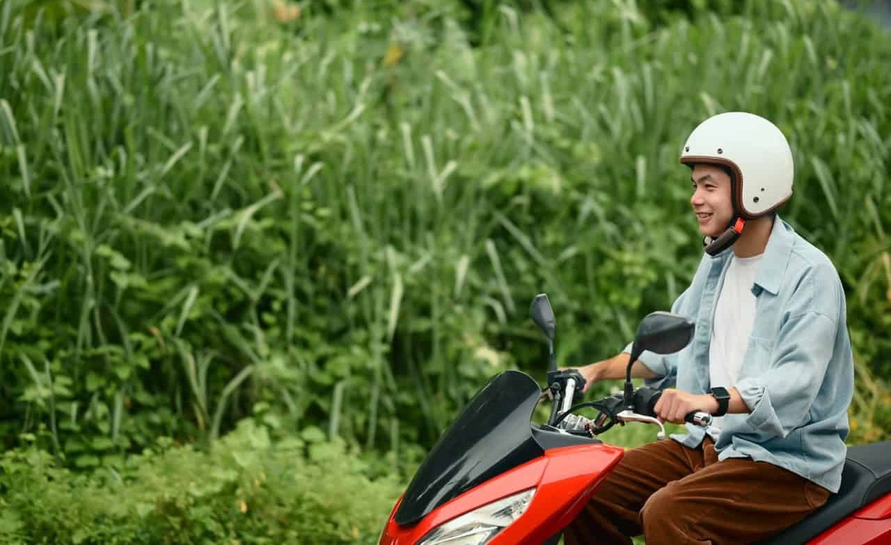 Young man riding a red motorcycle while smiling, representing new riders who often pay higher insurance rates due to limited experience.