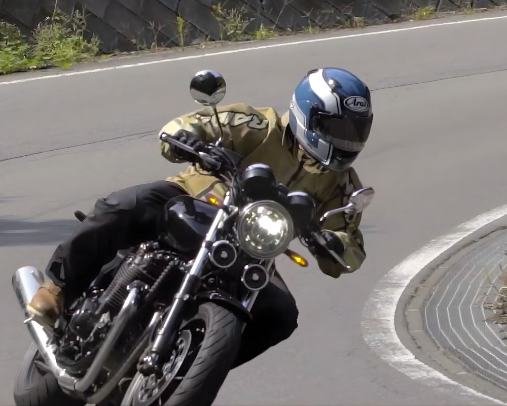 Rider wearing Arai Regent-X helmet leaning into a corner on a naked motorcycle