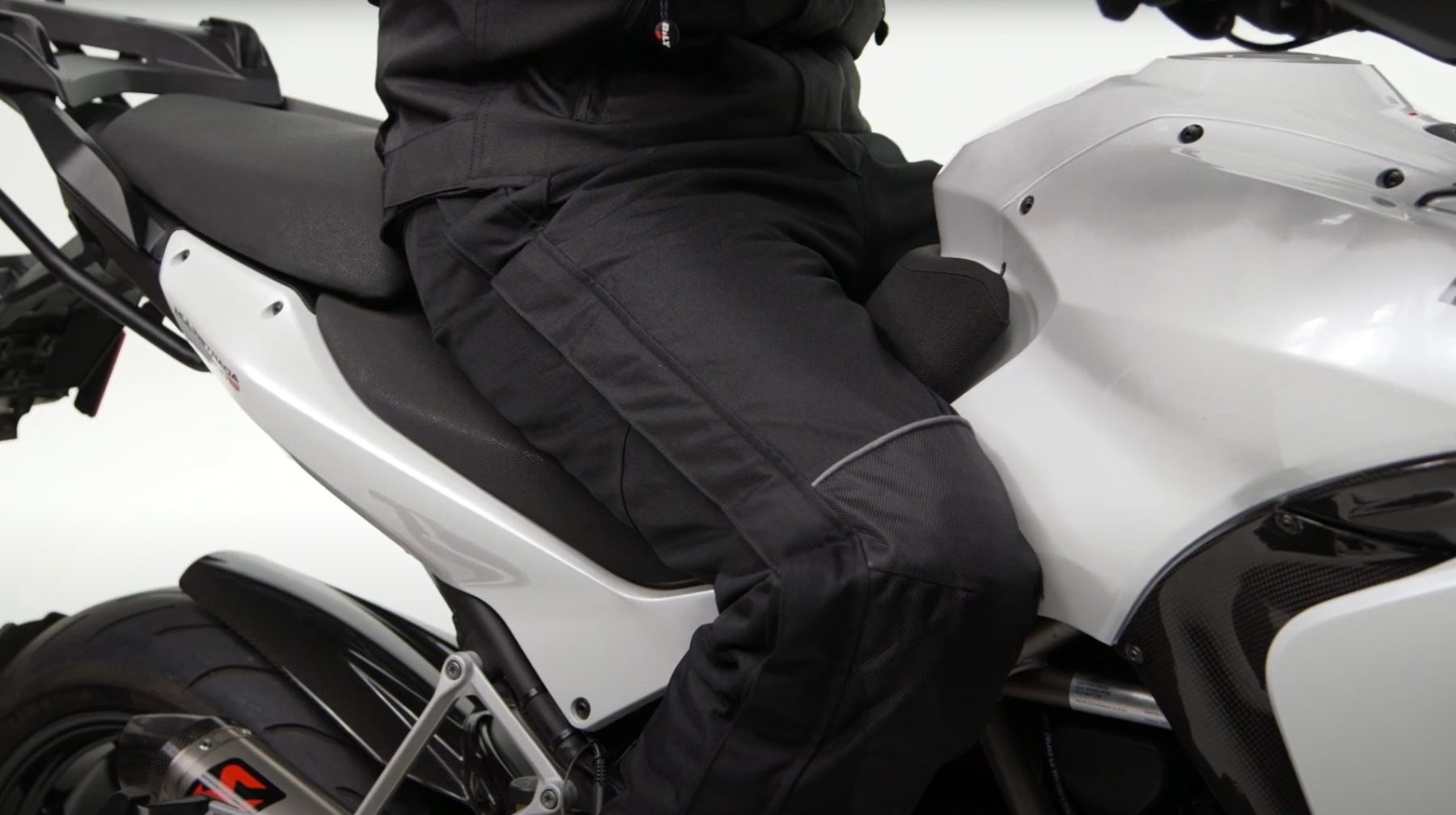 Rider wearing BILT Storm 2 waterproof overpants sitting on a motorcycle, showing reinforced panels and weather protection