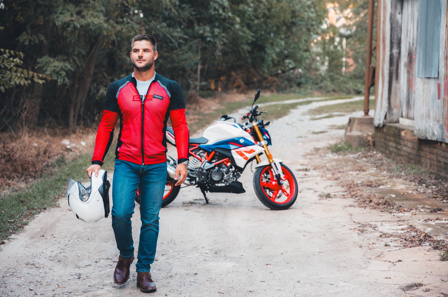 Rider wearing a breathable armored base layer shirt walking beside a motorcycle while holding a helmet outdoors