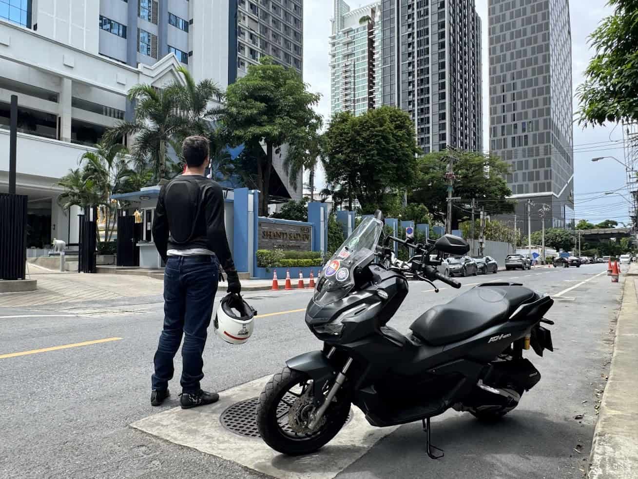 Urban rider standing beside a scooter holding a helmet on a city street