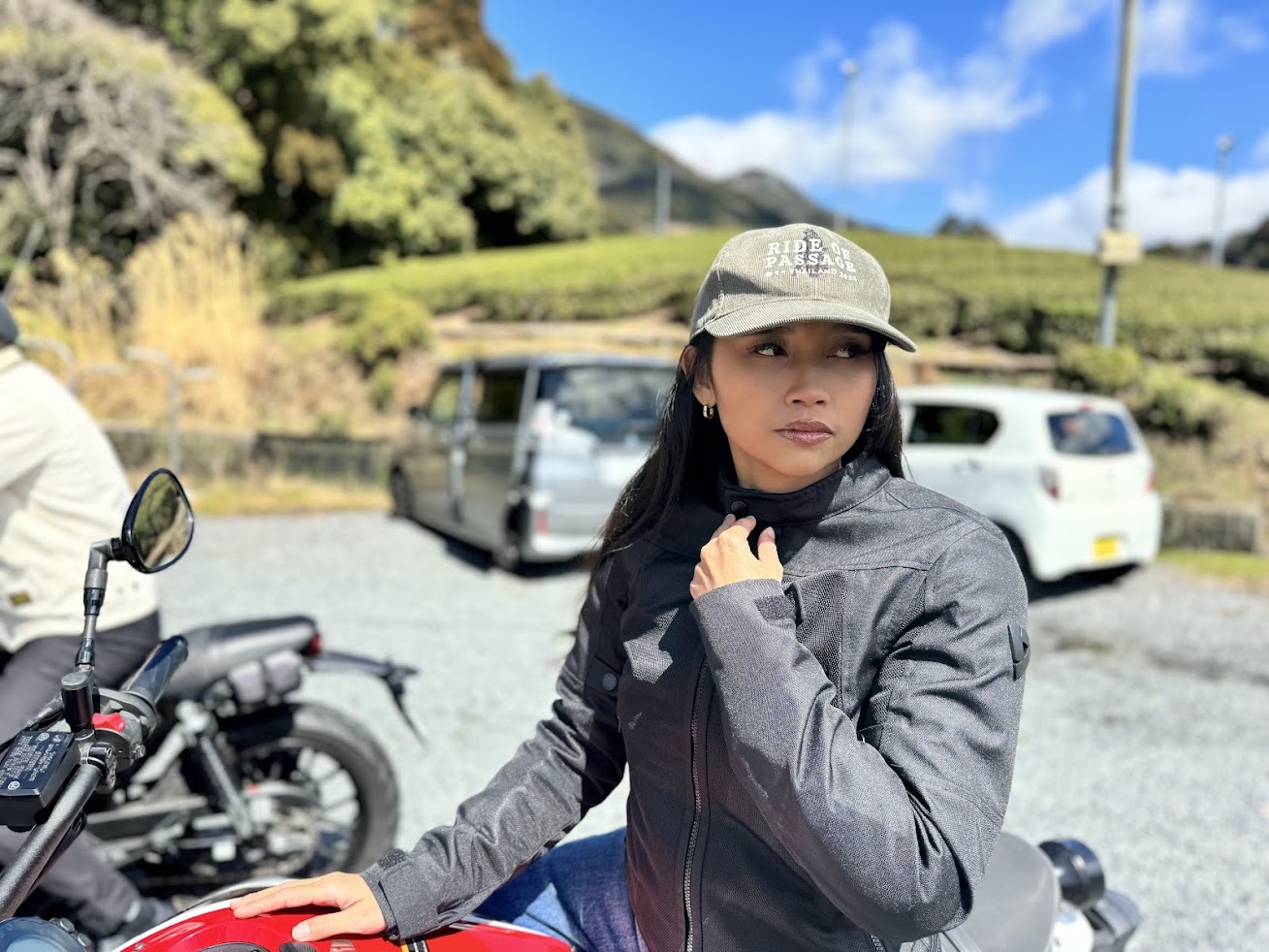 Woman wearing a black motorcycle riding jacket standing beside a red motorcycle