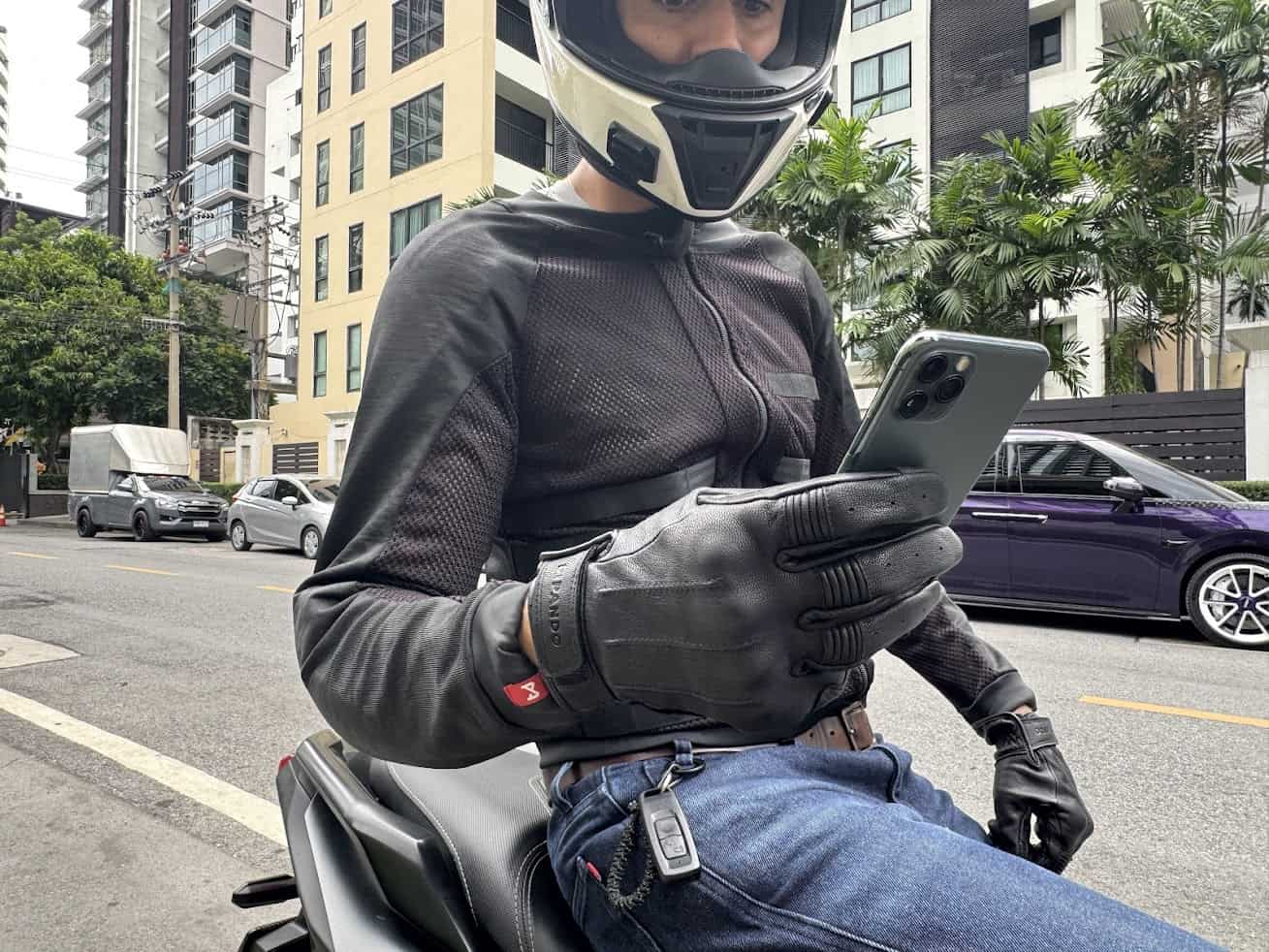 Rider wearing leather motorcycle gloves using a smartphone while seated on a motorcycle