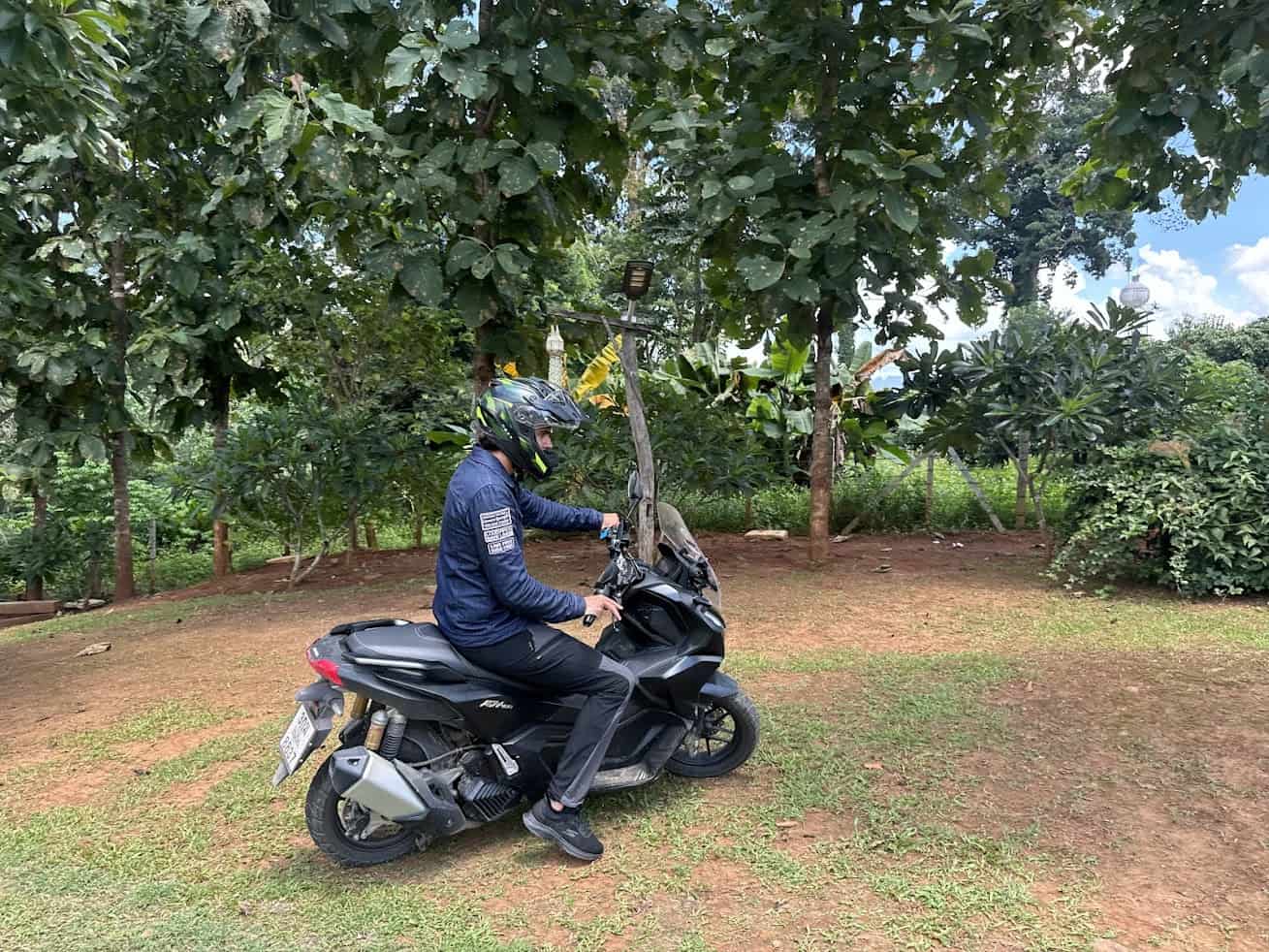 Rider wearing helmet sitting on a scooter in a tropical setting, demonstrating lightweight motorcycle gear suitable for hot climates
