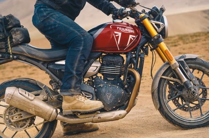 Rider wearing REAX 267 single-layer riding jeans on a Triumph motorcycle in a dusty outdoor setting