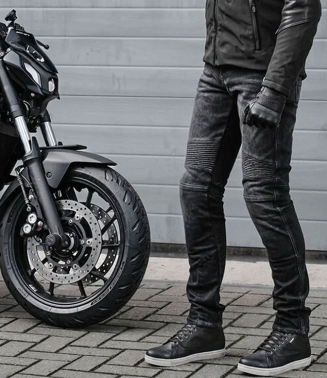 Rider wearing REV'IT! Moto 2 slim motorcycle riding jeans next to a black motorcycle