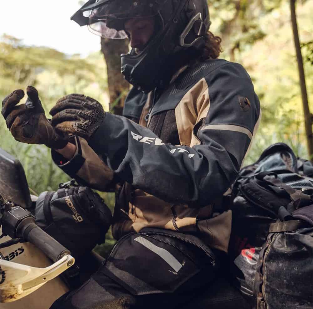 Rider wearing REV'IT Sand 5 gloves adjusting fit on adventure motorcycle