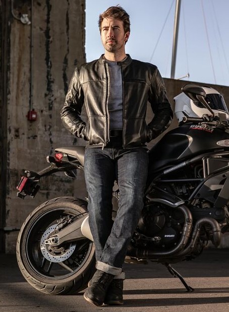 Rider wearing protective motorcycle jeans standing beside a bike, highlighting armored riding gear in a casual style