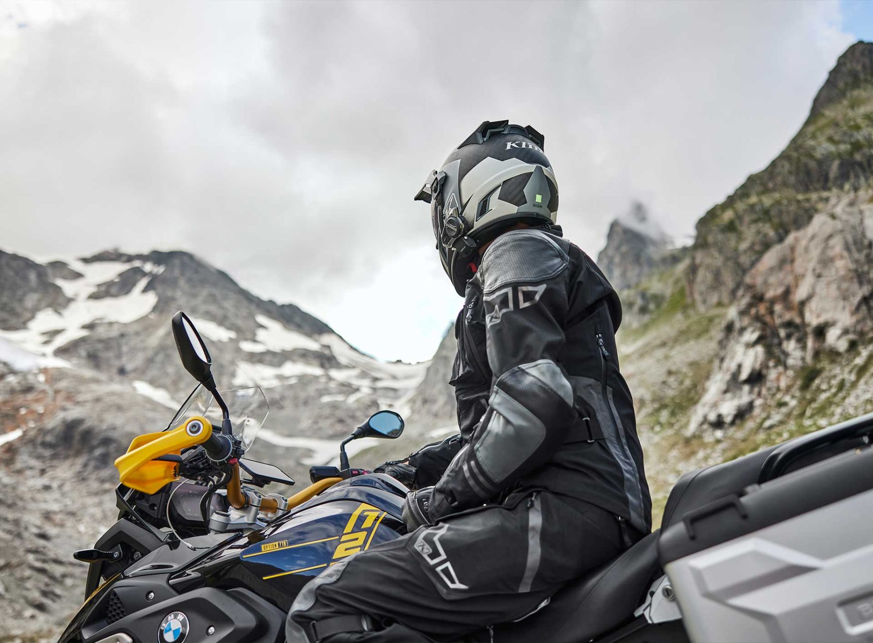 Rider wearing Klim Krios Pro helmet on an adventure motorcycle in mountainous terrain